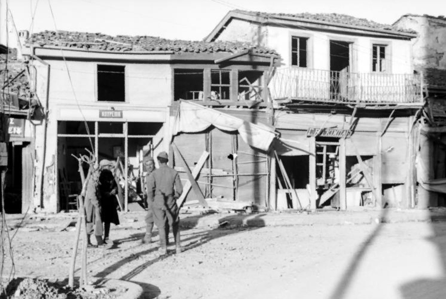 Deutsche Wehrmachtsangehörige und griechische Zivilist*innen vor zerstörten Häusern